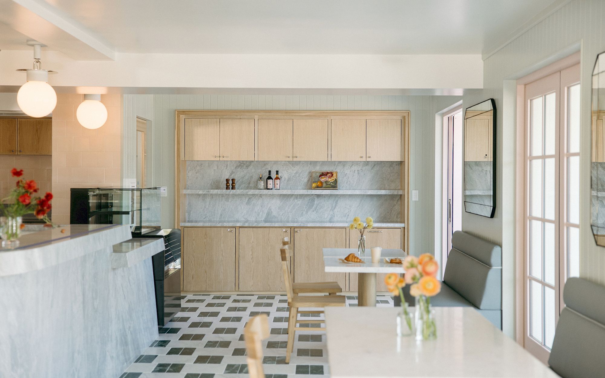 A bright modern kitchen with wooden cabinets, marble backsplash, pendant lights, and a dining table set with flowers.