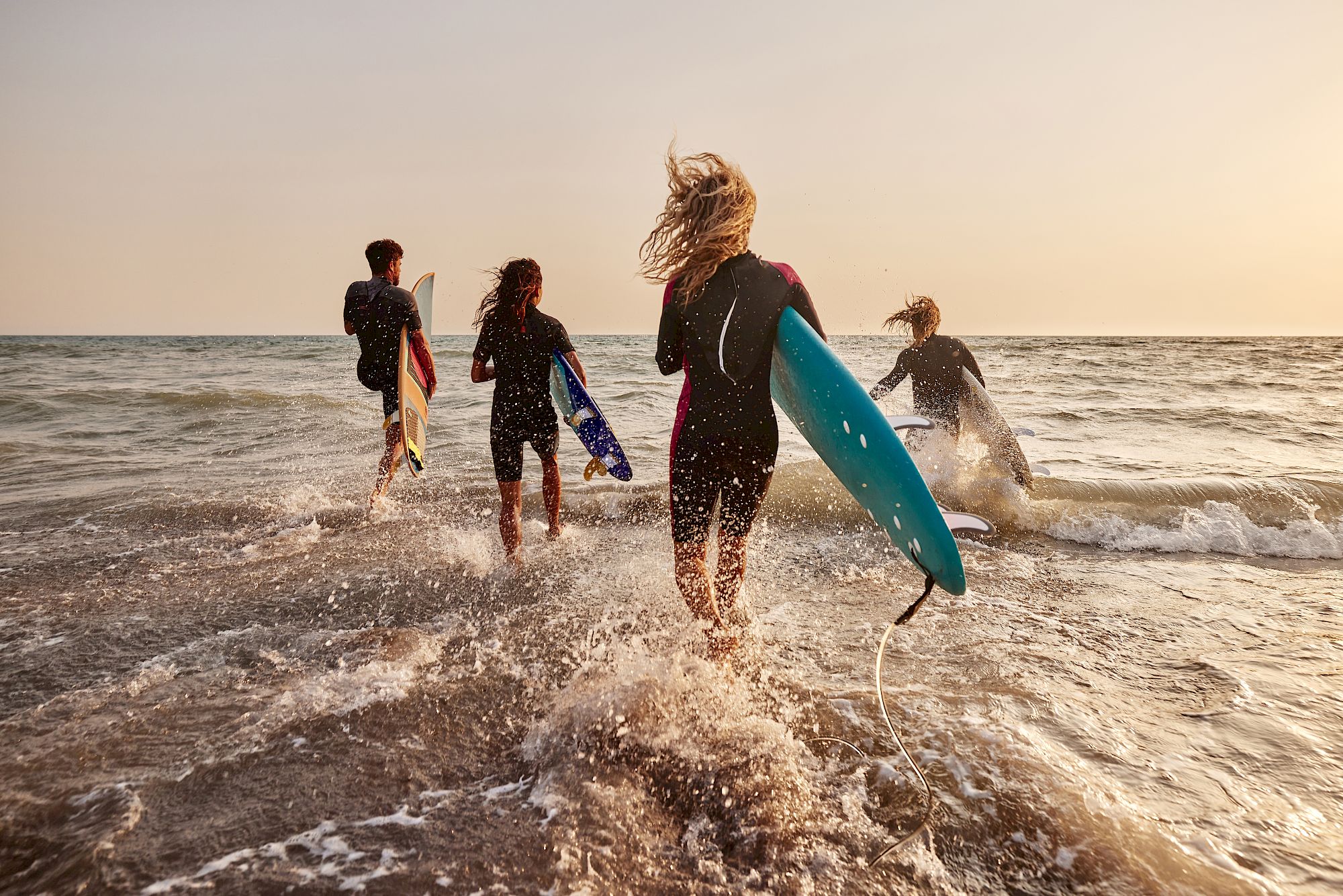 A group of surfers sprint across the shoreline holding surfboards as ocean waves crash behind them.