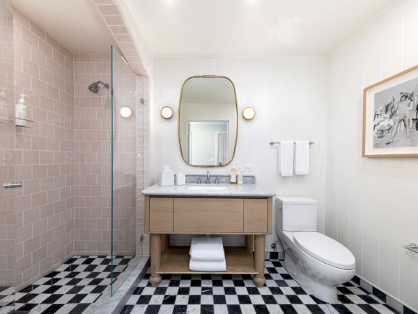 A bright modern bathroom with a glass shower, vanity mirror, marble sink, towels, and a white toilet.