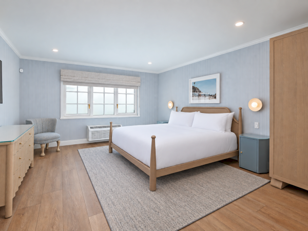 A modern bedroom with a wooden bed, striped walls, large window, rug, dresser, and bedside lamps.
