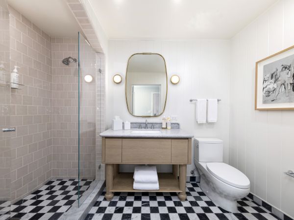 Bright modern bathroom with a glass shower, vanity, round lights, towel bar, and toilet.