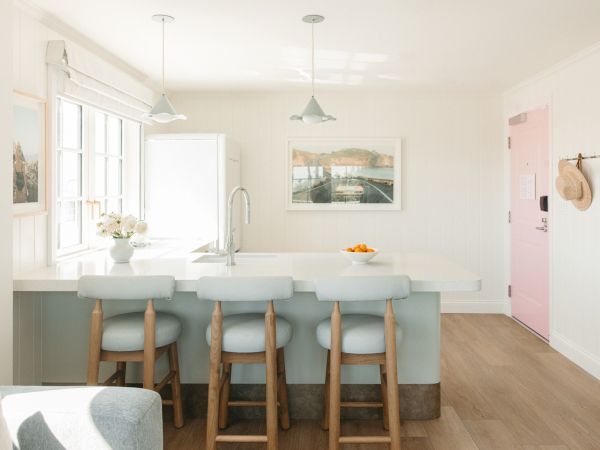 Bright modern kitchen with island and stools, pendant lights, sink and window, a framed seaside photo, and a hat display.