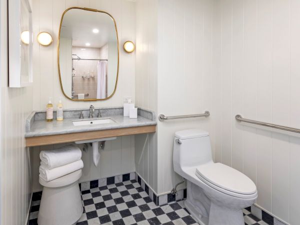 A modern bathroom with a marble vanity, round wall lights, an oval mirror, a toilet, and black-and-white checkered tile floors.