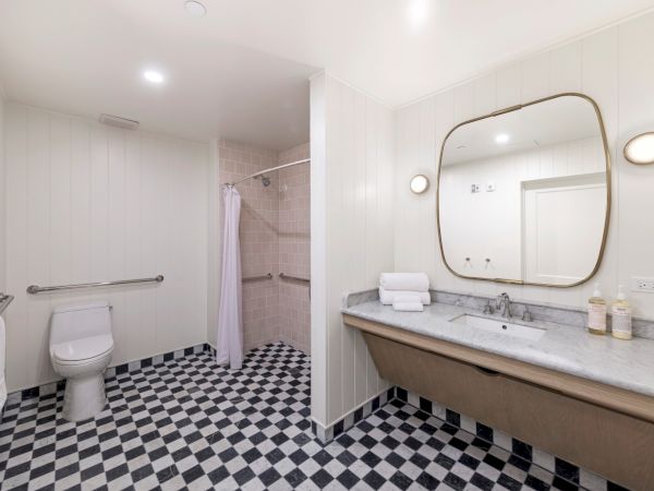 A modern bathroom with a toilet, glass shower, marble vanity, and a large round mirror.