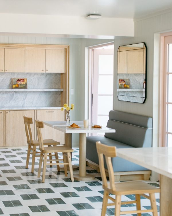 A bright modern kitchen-dining area with wooden cabinets, a small table and chairs, a gray sofa, and a large wall mirror.