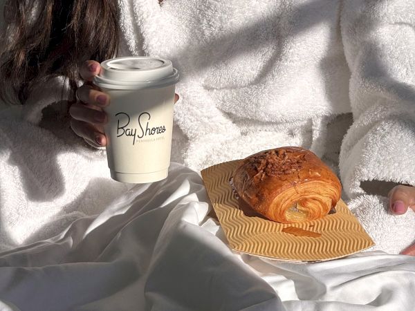 Coffee break at Bay Shores Peninsula Hotel&mdash;holding a to-go cup while a flaky croissant sits nearby.