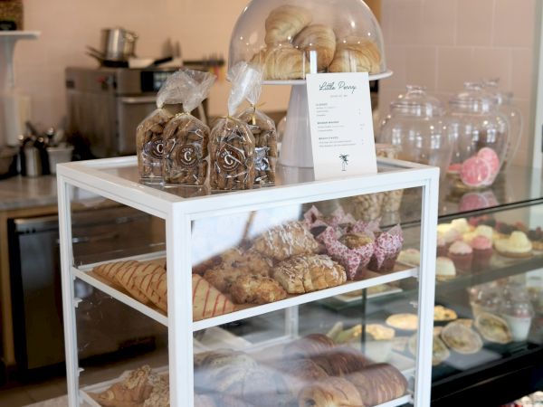 A bakery display case with wrapped croissants and cookies under glass domes in a bright kitchen.
