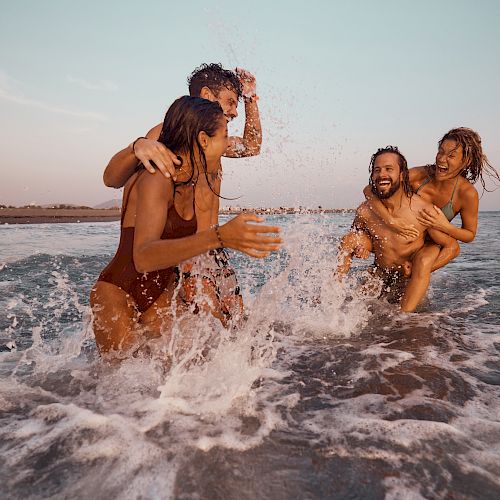 Friends laughing as they splash through ocean waves in the late-day sun.