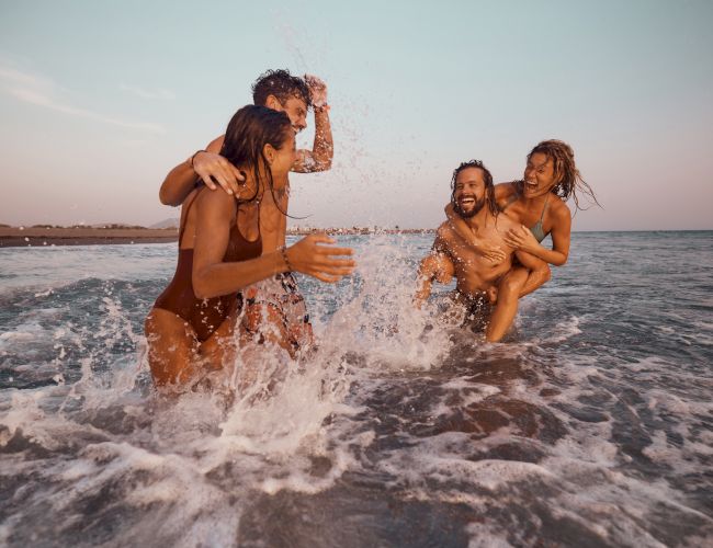 Friends laughing as they splash through ocean waves in the late-day sun.