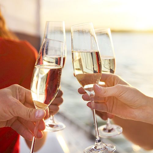 Friends clink sparkling champagne flutes in a sunny toast, with hands reaching for a celebratory cheers.