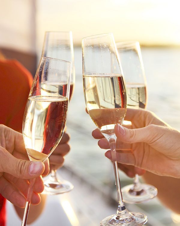 Friends clink sparkling champagne flutes in a sunny toast, with hands reaching for a celebratory cheers.