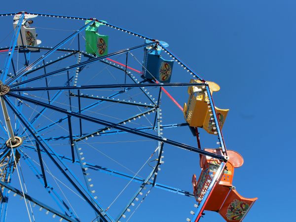 A close-up of a blue ferris wheel with colorful carved gondolas against a clear blue sky.