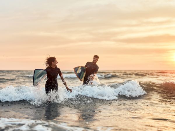 Two surfers ride choppy waves at sunset, boards cutting through the spray near the shoreline.
