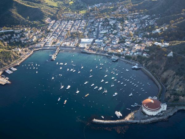 Aerial view of a hillside coastal town with a busy marina packed with yachts and sailboats in a sheltered bay.