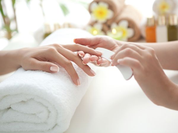 A spa therapist massages a client&rsquo;s hands on a soft towel, with a calm home-like background blurred.
