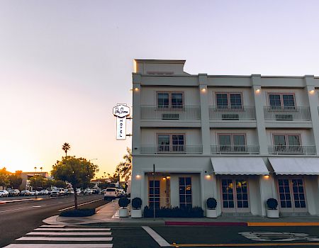 Bay Shores Hotel façade with lit windows, balcony railings, street parking, and a sign by the sidewalk at dusk.