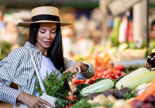 A woman in a straw hat arranges fresh herbs at a colorful outdoor market stall.