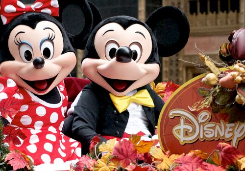 Minnie and Mickey Mouse pose at a Disney fall-themed display with colorful autumn leaves and decorations.