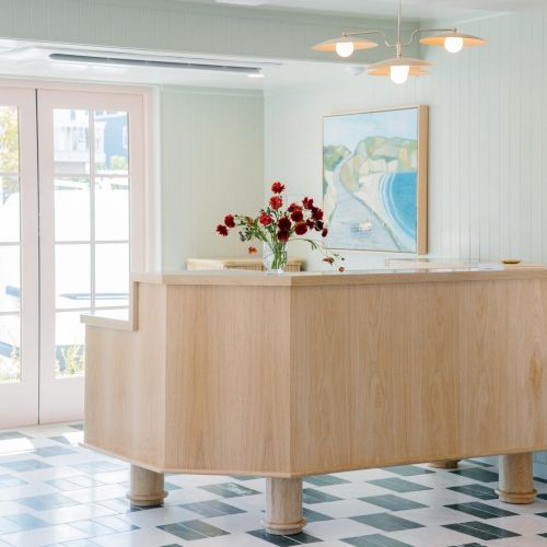 Bright lobby with a wooden reception counter, red flowers, wall art, pendant lights, and large windows, welcoming you in.