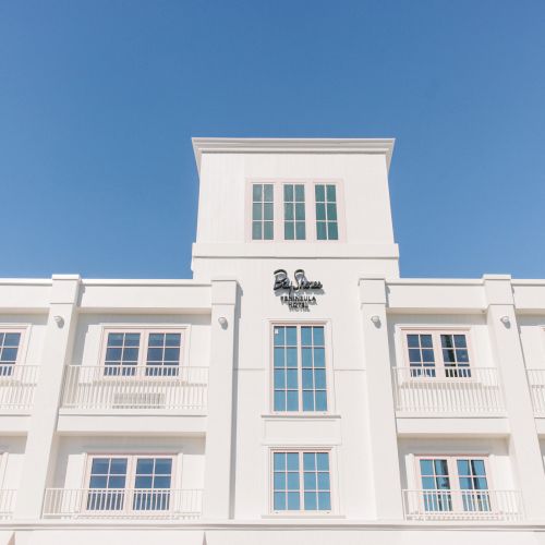 A white multi-story hotel building with balconies and the &ldquo;Bay Shores&rdquo; signage against a clear blue sky.