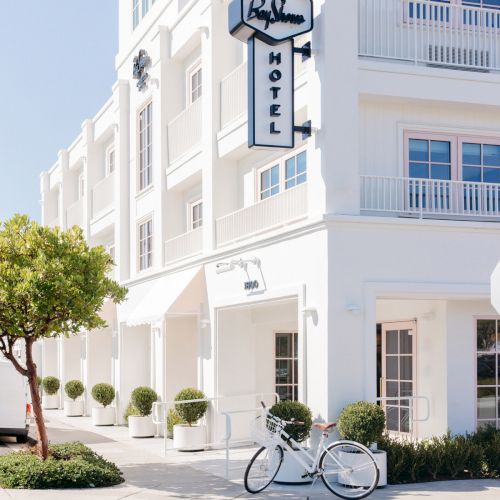A white hotel building with a sign reading &ldquo;Bay Shore&rdquo; and &ldquo;HOTEL,&rdquo; plus a bicycle parked outside, under blue sky.