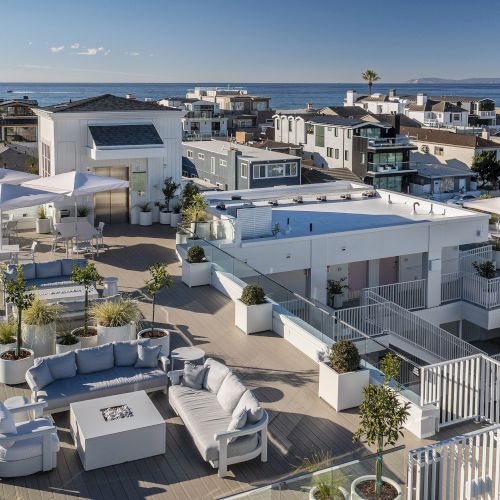Rooftop terrace with lounge seating, umbrellas, and a heated pool overlooking a coastal ocean and nearby houses.