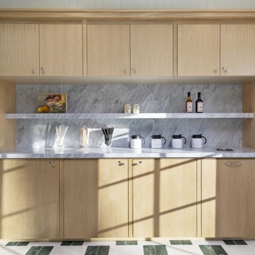 A kitchen counter display with open wooden cabinets, jars and glass containers, wine bottles, and a marble backsplash.