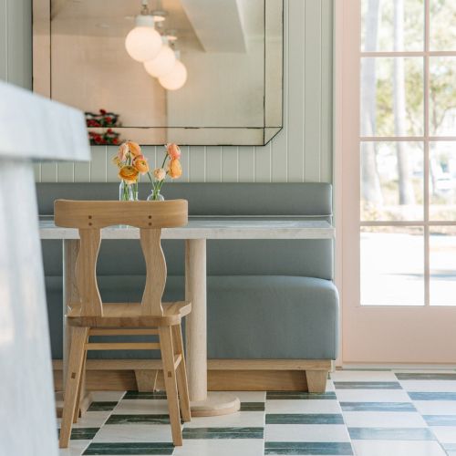 Cozy room corner: wooden stool with peach flowers beside a blue bench, reflected in a large wall mirror.