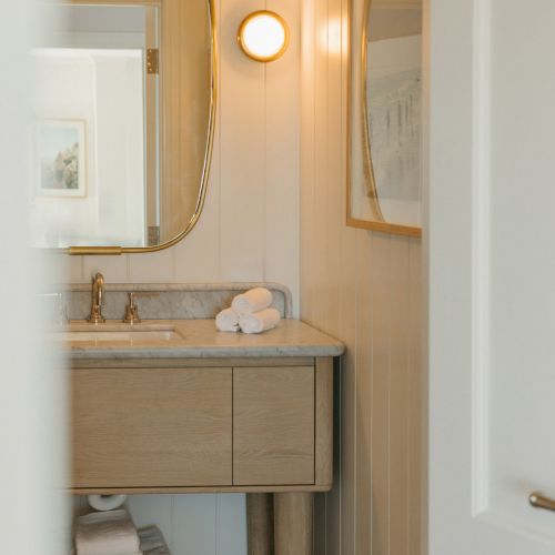 A modern bathroom with a marble sink vanity, warm round mirror light, and neatly folded white towels.