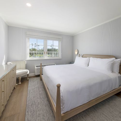 A bright, modern bedroom with a large bed, nightstand, dresser, window with blinds, and a ceiling light.
