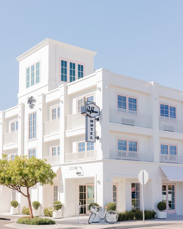 A white multi-story hotel facade with balconies and hanging &ldquo;HOTEL&rdquo; signage, plus a small street sign and bicycle out front.