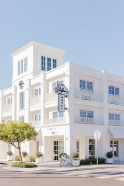 A white multi-story hotel facade under a clear sky, with a vertical &ldquo;Bicycle&rdquo; sign and a parked bicycle in front.