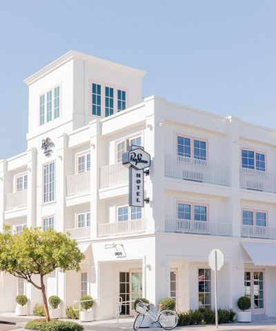 A white multi-story hotel facade under a clear sky, with a vertical &ldquo;Bicycle&rdquo; sign and a parked bicycle in front.