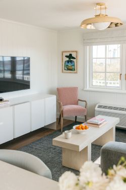 A bright living room with a TV, a striped armchair, coffee table, oranges, and a gold ceiling lamp by the window.