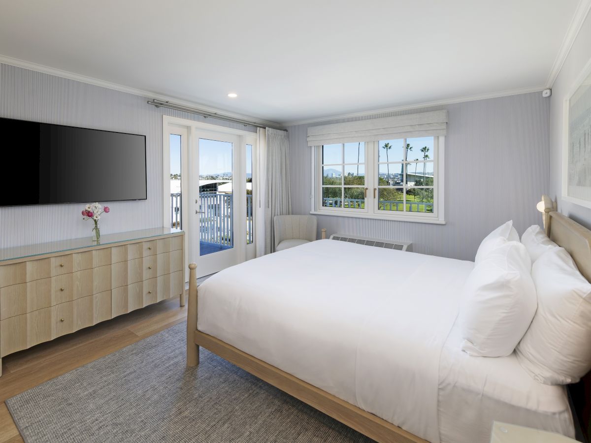 Bright modern bedroom with a large bed, striped walls, TV on a dresser, and patio doors with curtains.